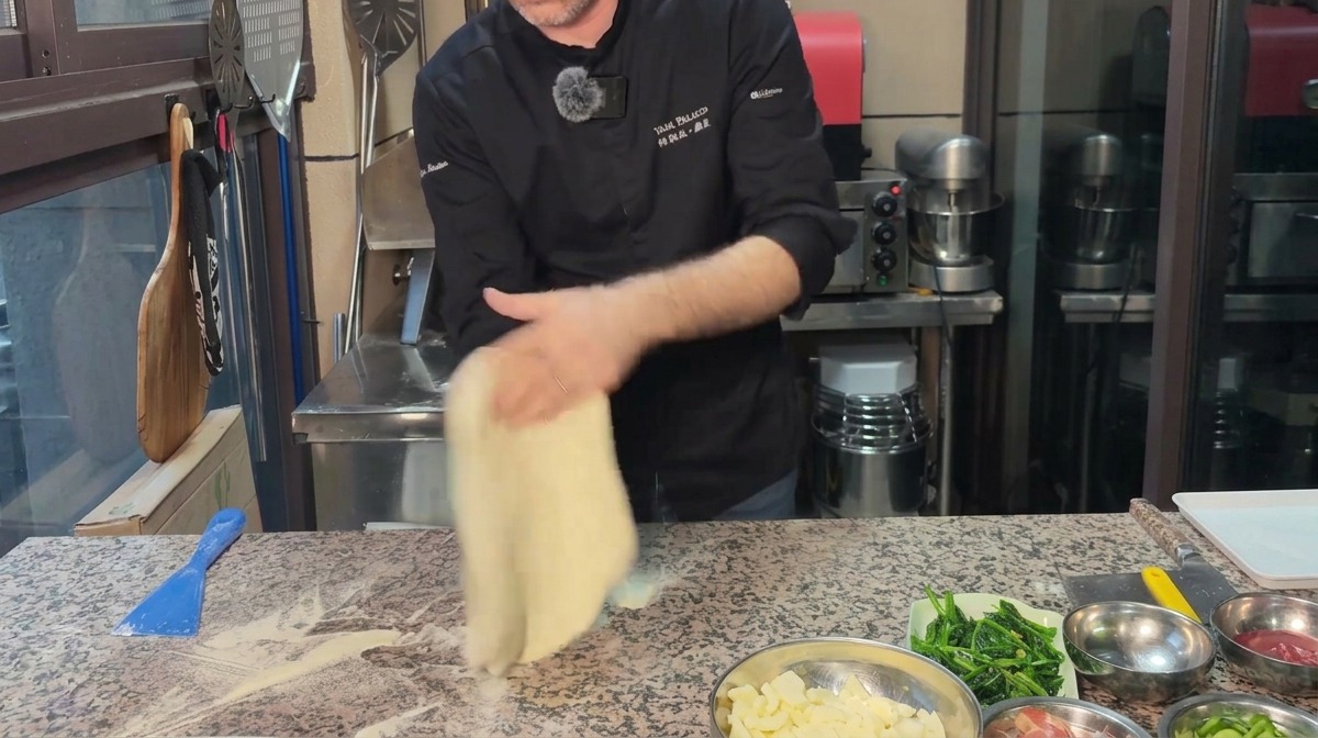 Ein Koch formt Pizzateig auf einer bemehlten Marmorplatte zu einem gleichmäßigen Kreis.