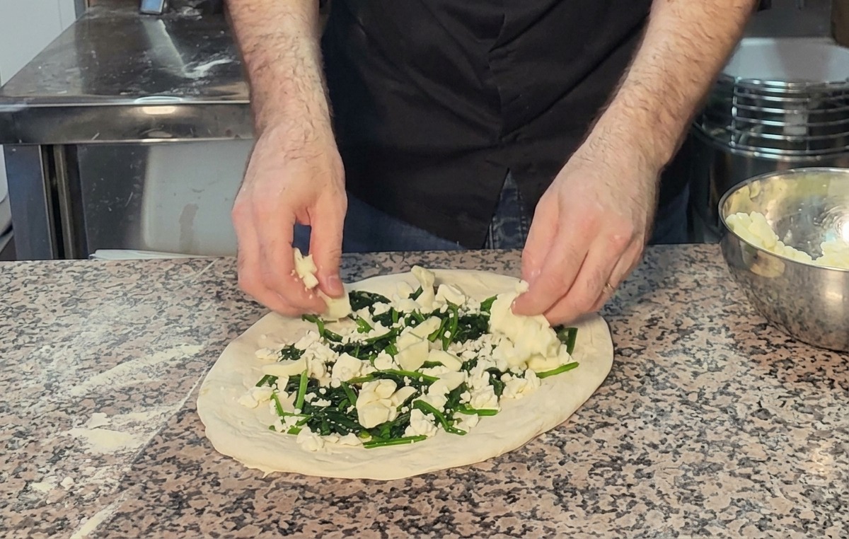 Geriebener Mozzarella wird auf die Pizza mit Spinat und Feta gestreut.