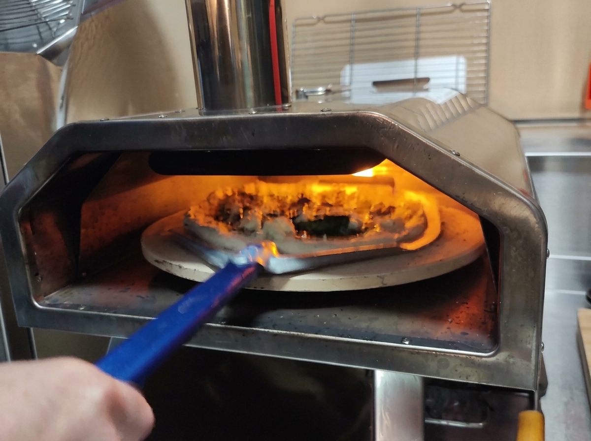 Ein perforierter Pizzaschieber hebt die vorbereitete Pizza in einen brennenden Ofen.