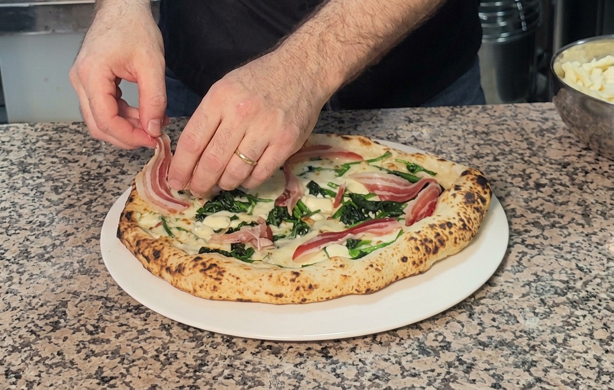 Dünne Pancetta-Scheiben werden auf die frisch gebackene, heiße Pizza drapiert.
