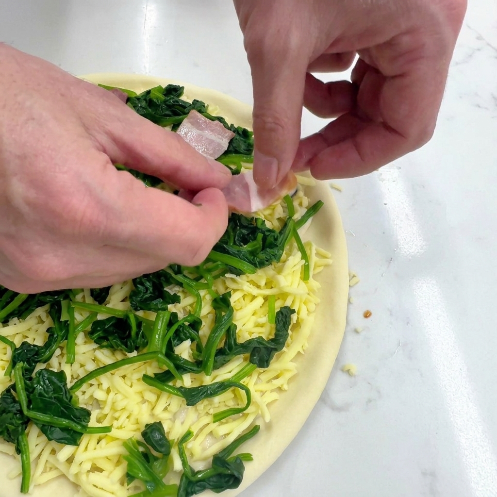 Hände legen vorsichtig rohe Speckstreifen auf die Pizza mit Spinat und Käse.