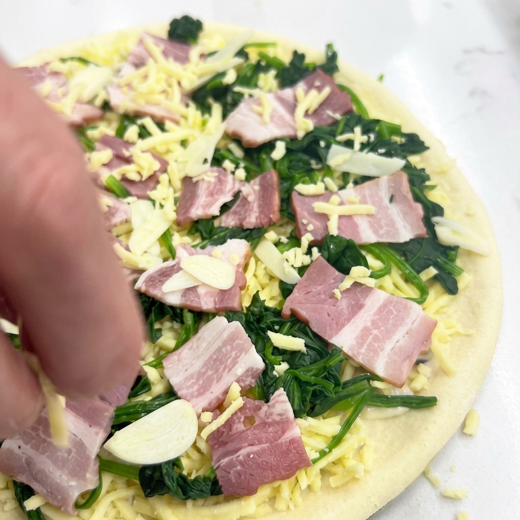 Eine Hand streut eine letzte Schicht Mozzarella über die Pizza mit allen Zutaten.