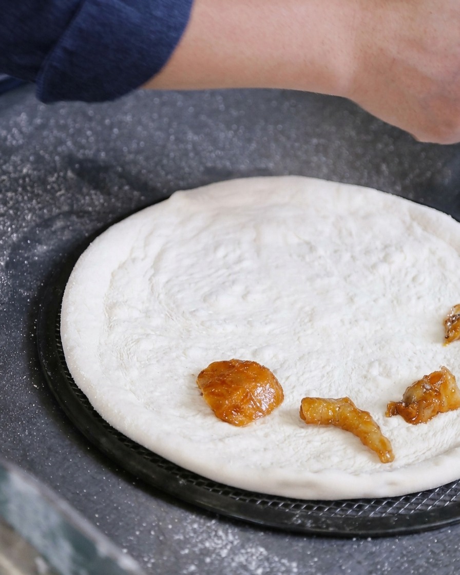 Eine Hand legt marinierte rohe Meeresfrüchte direkt auf einen dünn ausgezogenen weißen Pizzateig.