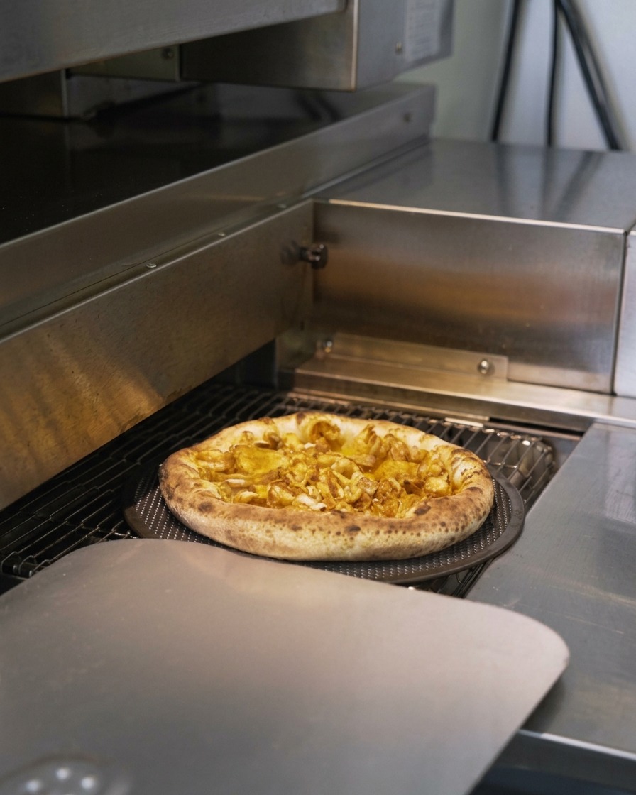 Eine Meeresfrüchte-Pizza fährt durch einen Durchlaufofen, wobei der Teigrand aufpufft und bräunt.