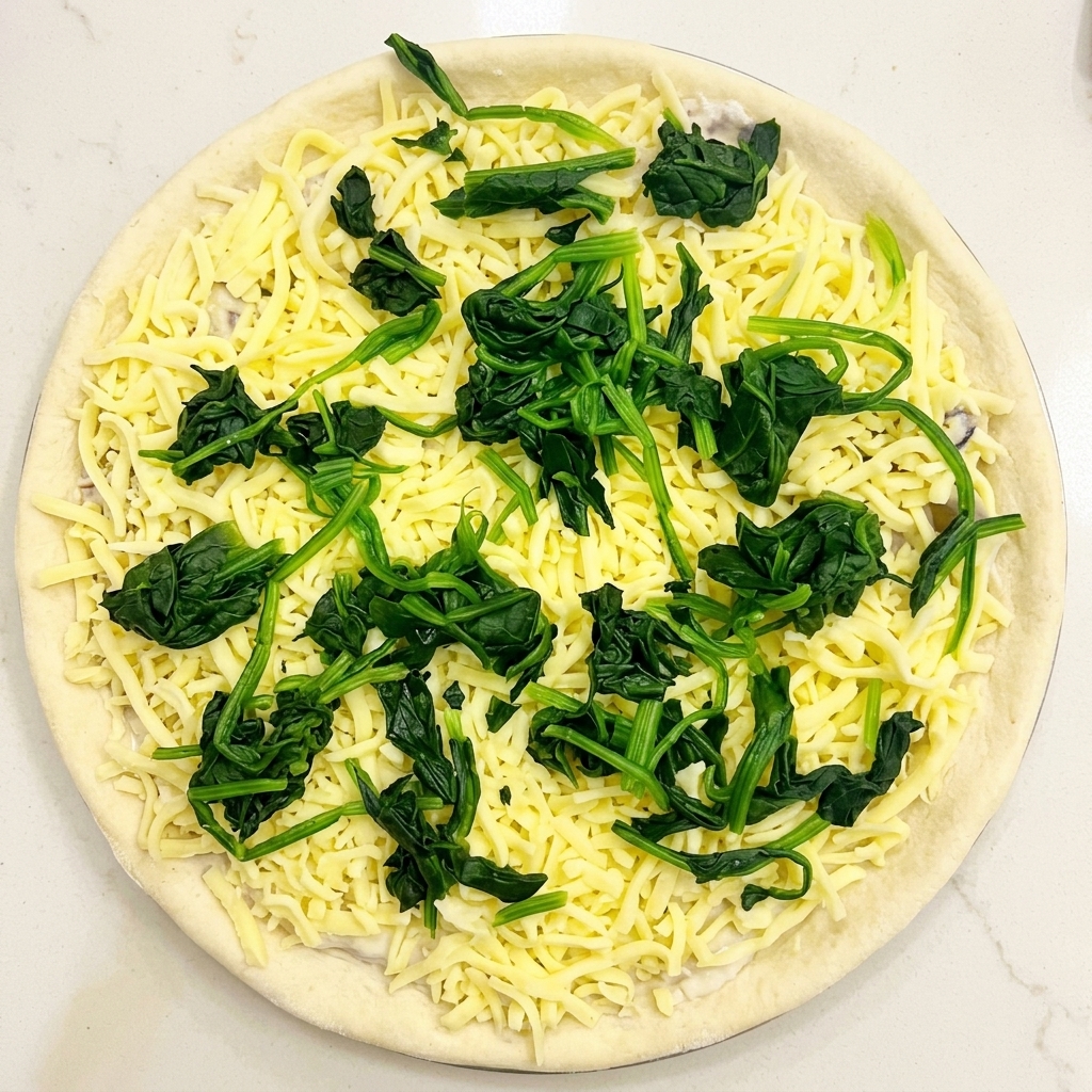 Draufsicht auf eine Pizza mit Sauce, Käse und gleichmäßig verteilten Häufchen von blanchiertem Spinat.