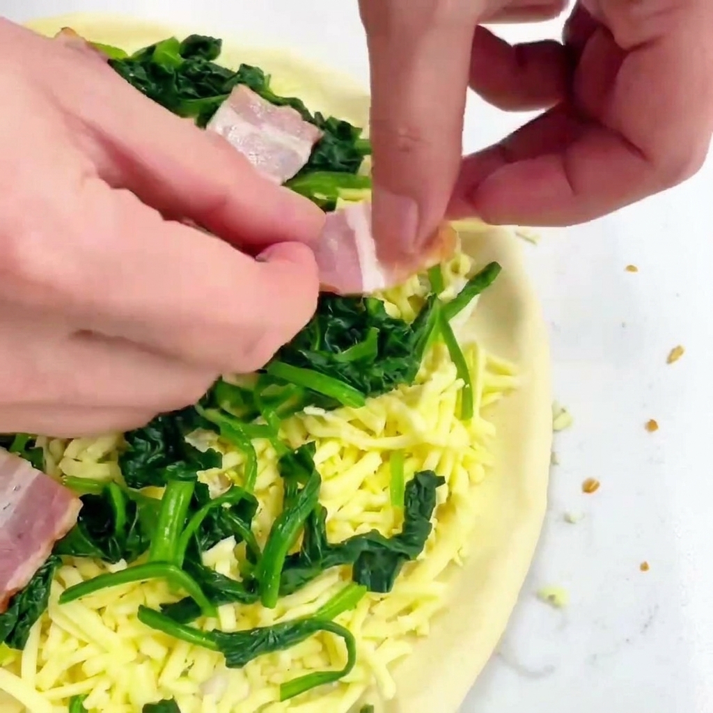 Hände legen quadratische Stücke von rohem Speck auf die Pizza mit Käse und Spinat.