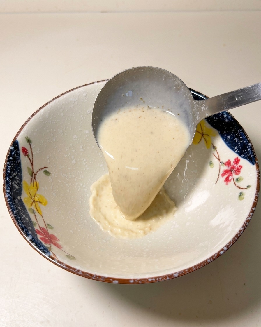 Eine Metallkelle gießt heiße, cremige Ramen-Brühe in eine gemusterte Keramikschüssel.