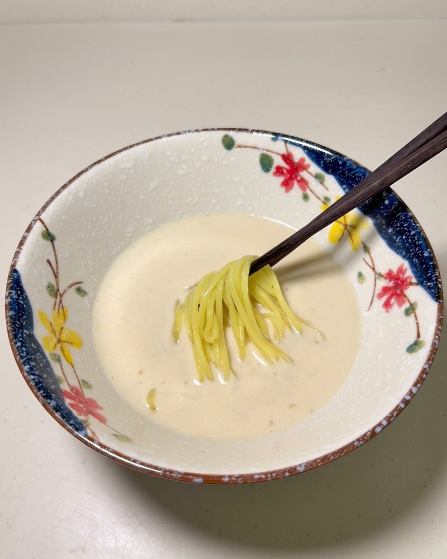 Gekochte gelbe Ramen-Nudeln werden vorsichtig in die cremige Suppenbasis in einer Schüssel gelegt.