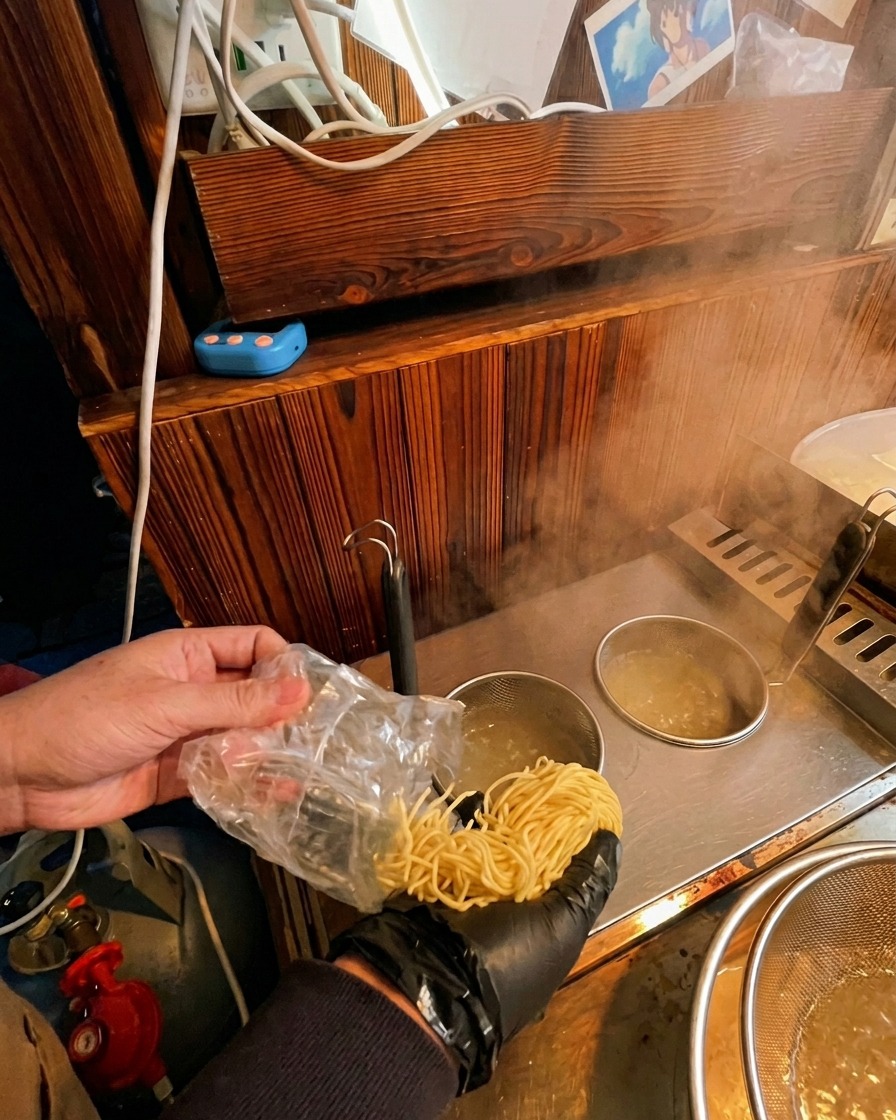 Frische Ramen-Nudeln werden aus einer Packung in ein Metallsieb in kochendes Wasser gegeben.