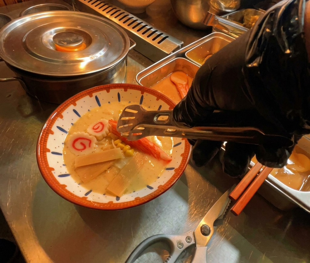 Eine Hand legt Scheiben von Narutomaki-Fischkuchen in die dampfende Ramen-Suppe.