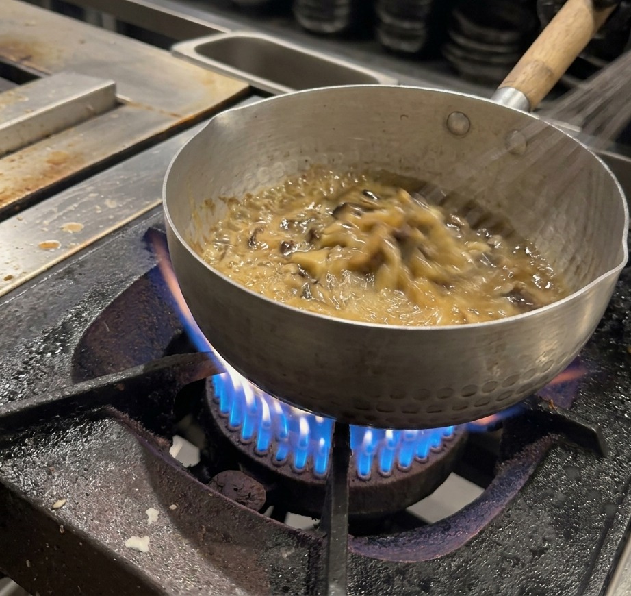 Ein Schneebesen rührt kräftig eine dicke, sprudelnde braune Sauce in einem Topf.
