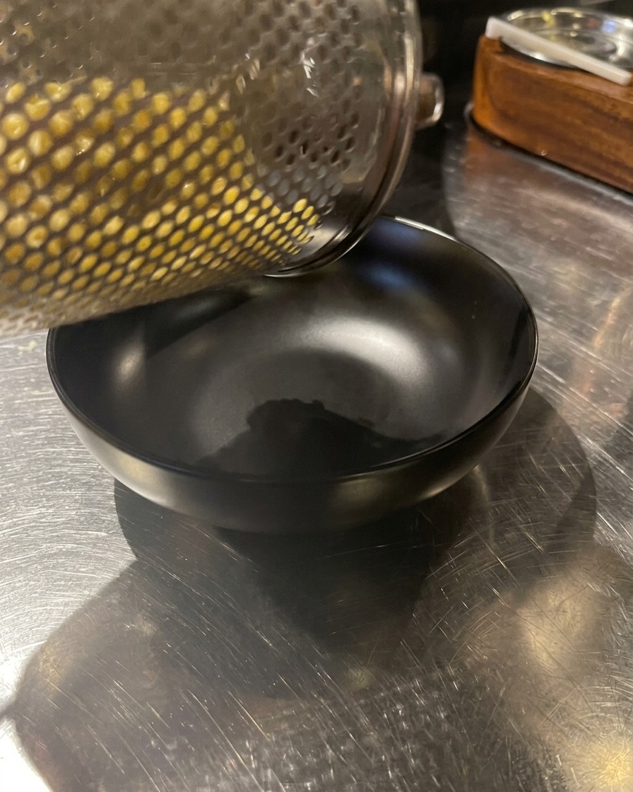 Frisch gekochte gelbe Nudeln werden aus einem Sieb in eine schwarze Schüssel gegeben.