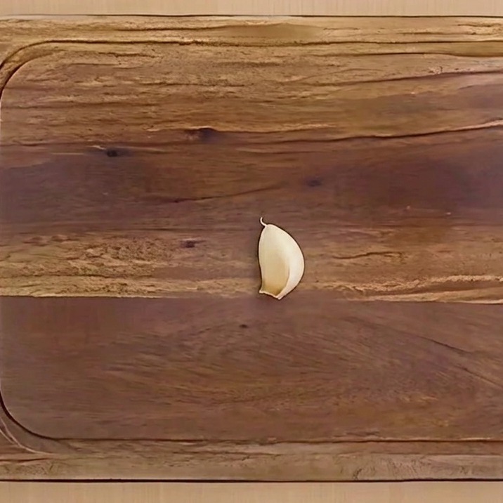 Eine geschälte Knoblauchzehe, der Länge nach halbiert, auf einem Holzschneidebrett.