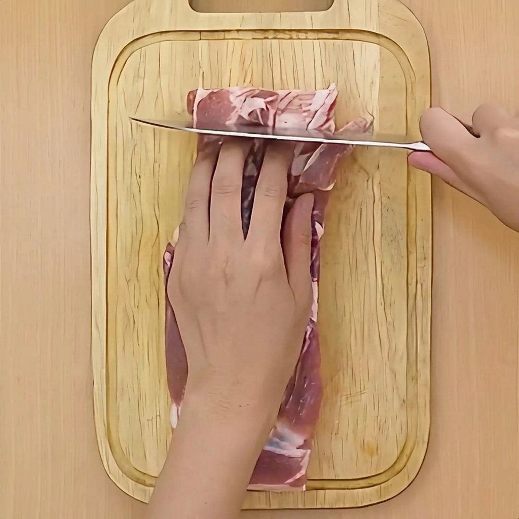 Ein Messer macht flache Schnitte in die Oberfläche eines Stücks Schweinebauch.