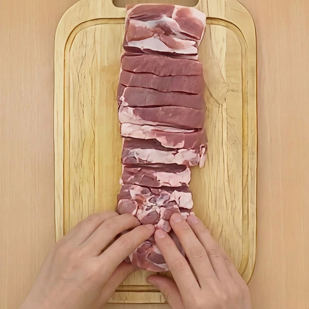 Zwei Hände rollen den Schweinebauch fest zu einem Zylinder zusammen.
