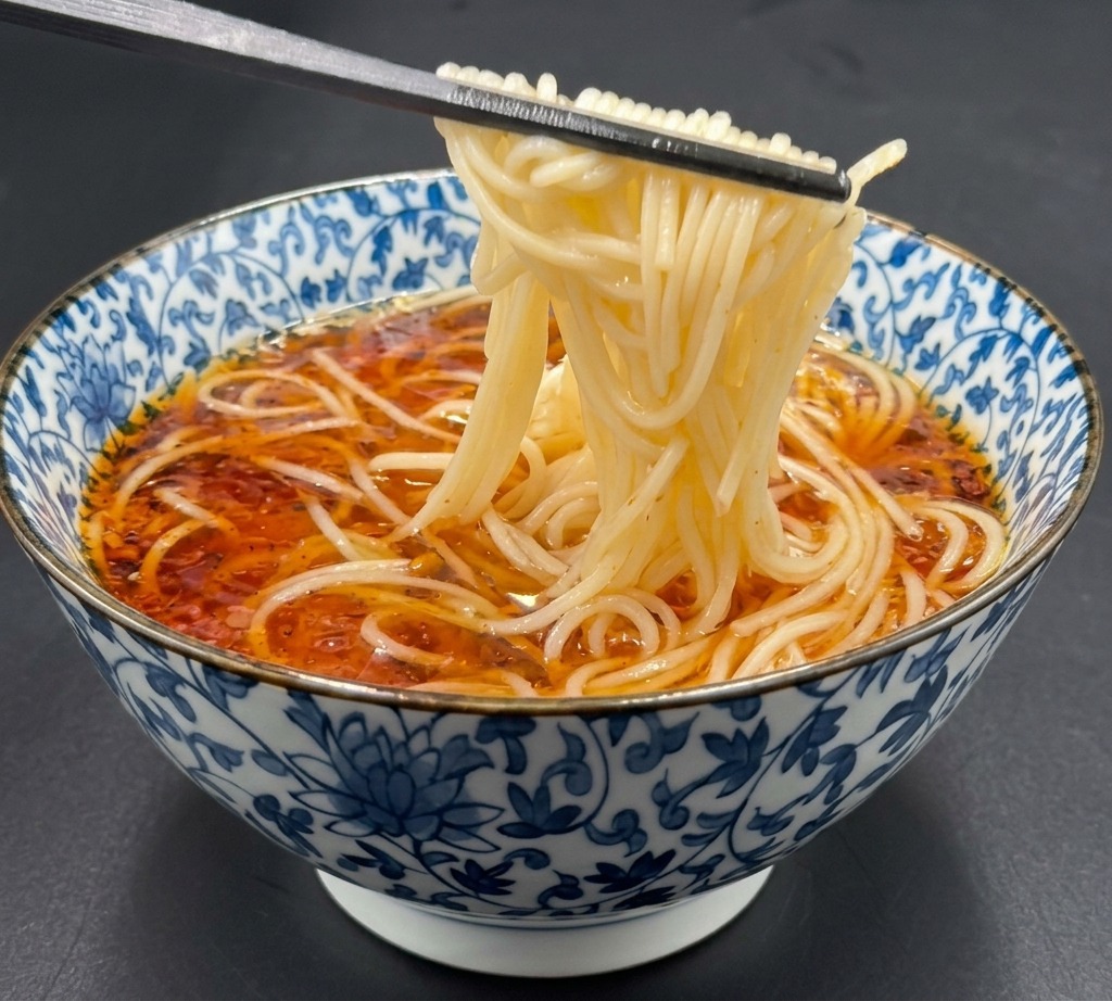 Stäbchen heben gekochte Ramen-Nudeln an und legen sie vorsichtig in die dunkle Brühe.
