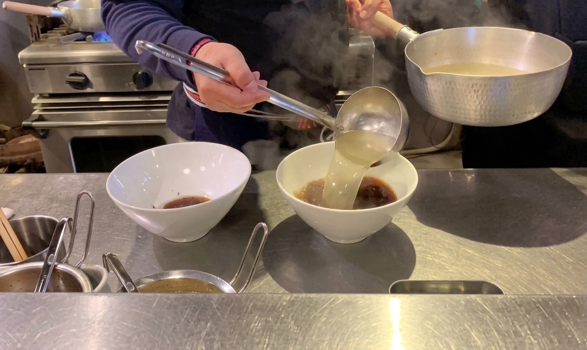 Dampfende, klare heiße Brühe wird über das dunkle Tare in die Ramen-Schüsseln gegossen.
