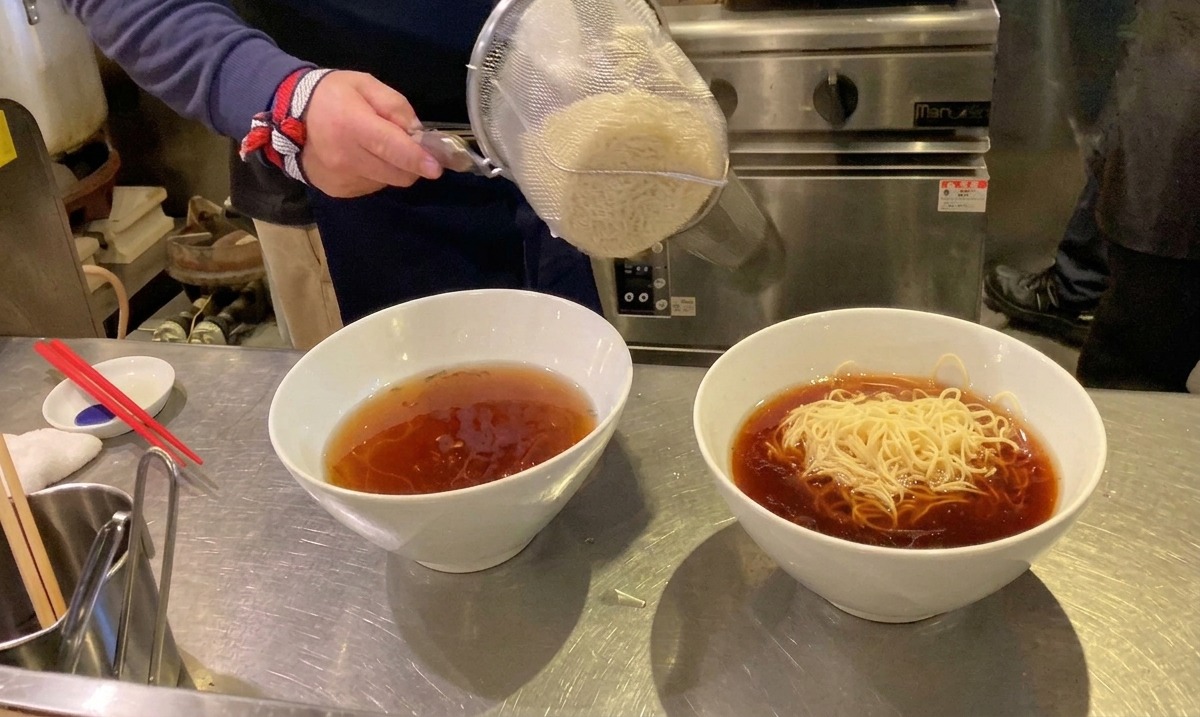 Frisch gekochte Ramen-Nudeln werden aus einem Sieb direkt in eine Schüssel mit heißer Suppe gegeben.