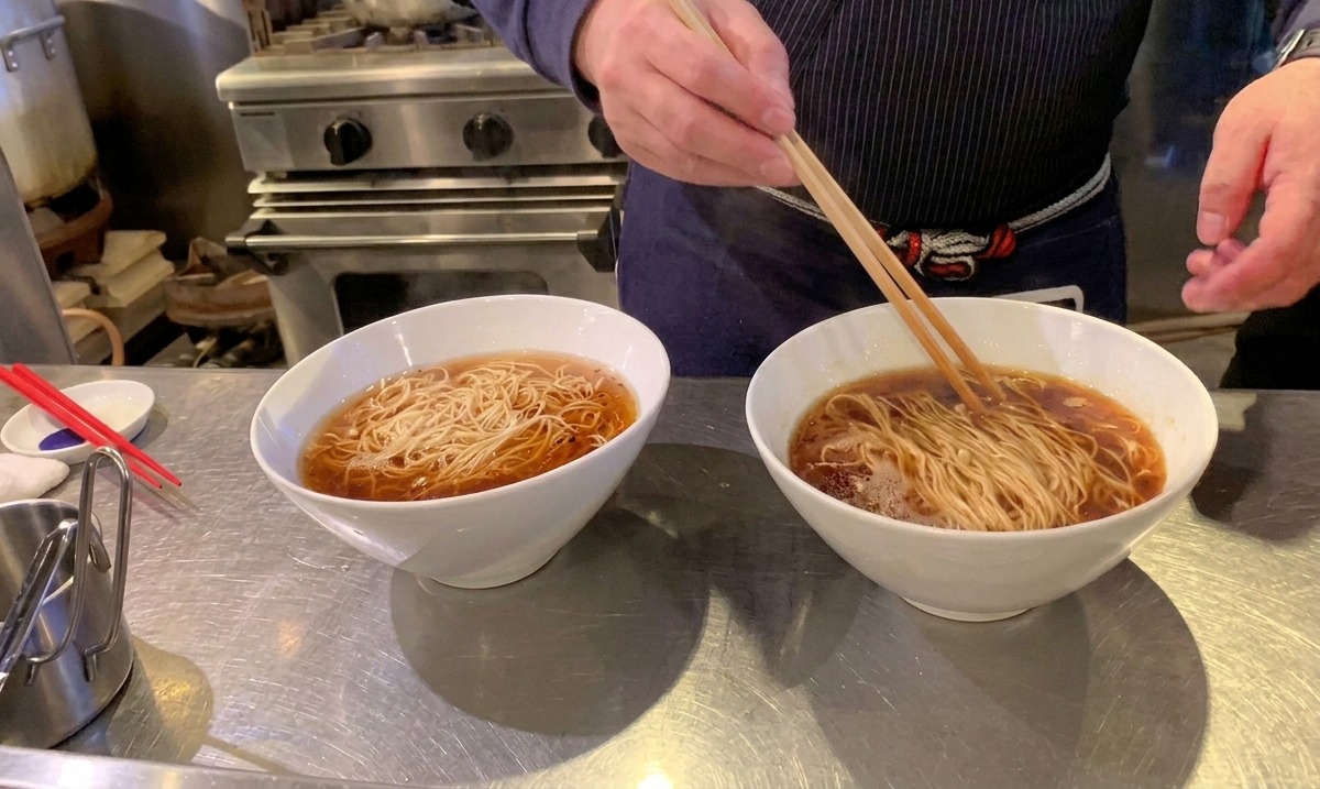Mit langen Holzstäbchen werden die Ramen-Nudeln ordentlich in der Brühe gefaltet und arrangiert.