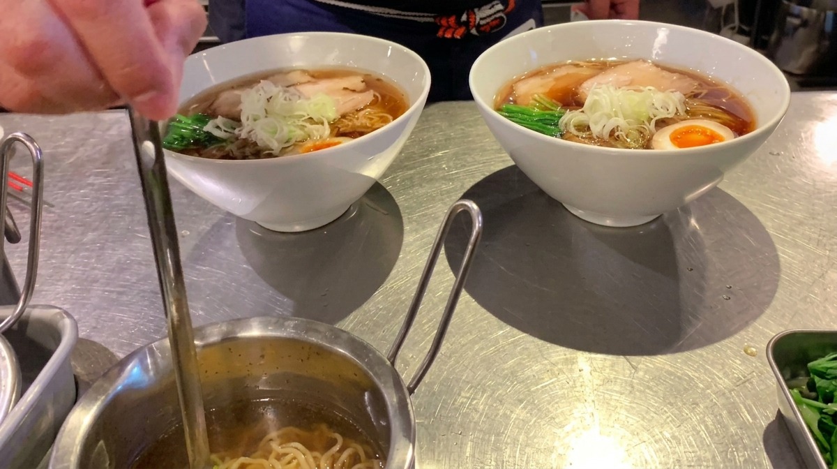 Eine kleine Kelle träufelt klares Aromaöl über eine fertige Schüssel Ramen.