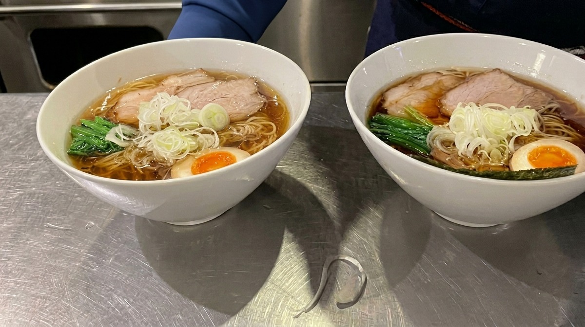 Ein quadratisches Blatt Nori-Alge wird als letzte Garnierung in den Rand einer Ramen-Schüssel gesteckt.