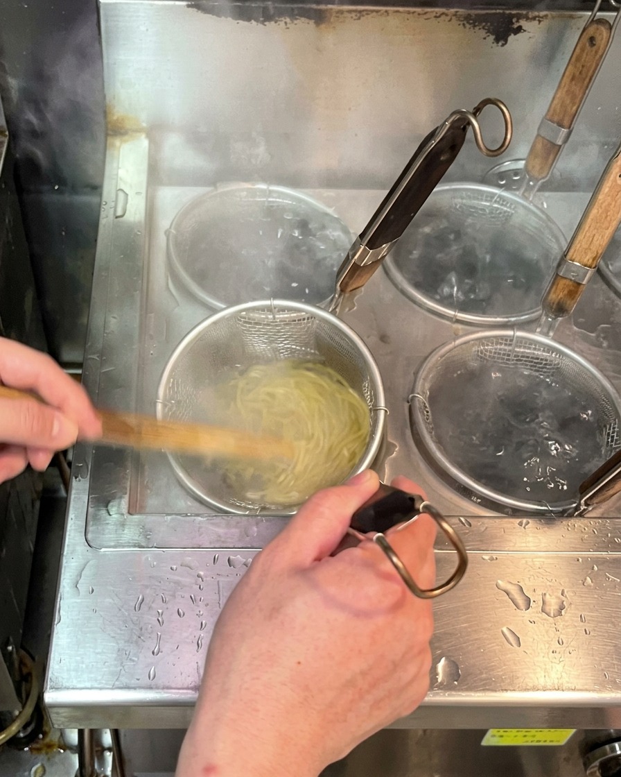 Frische gelbe Ramen-Nudeln garen in einem Nudelsieb in sprudelnd kochendem Wasser.