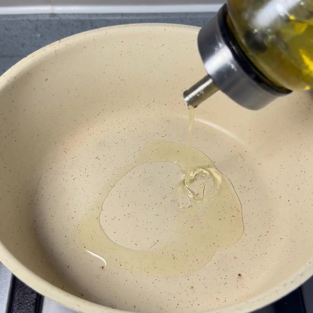 Neutrales Speiseöl wird aus einer Glasflasche in eine helle Pfanne gegossen.