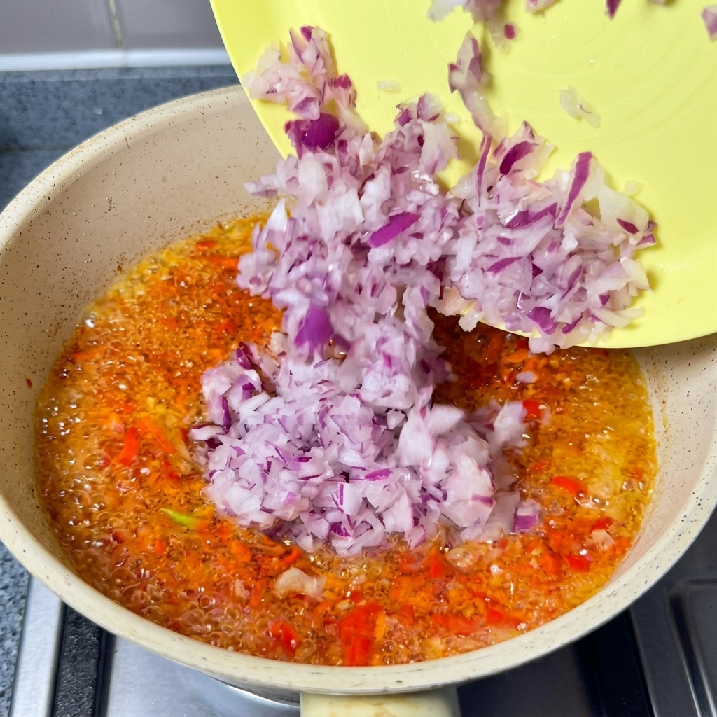 Gehackte rote Zwiebeln werden in das köchelnde Chiliöl gegeben.