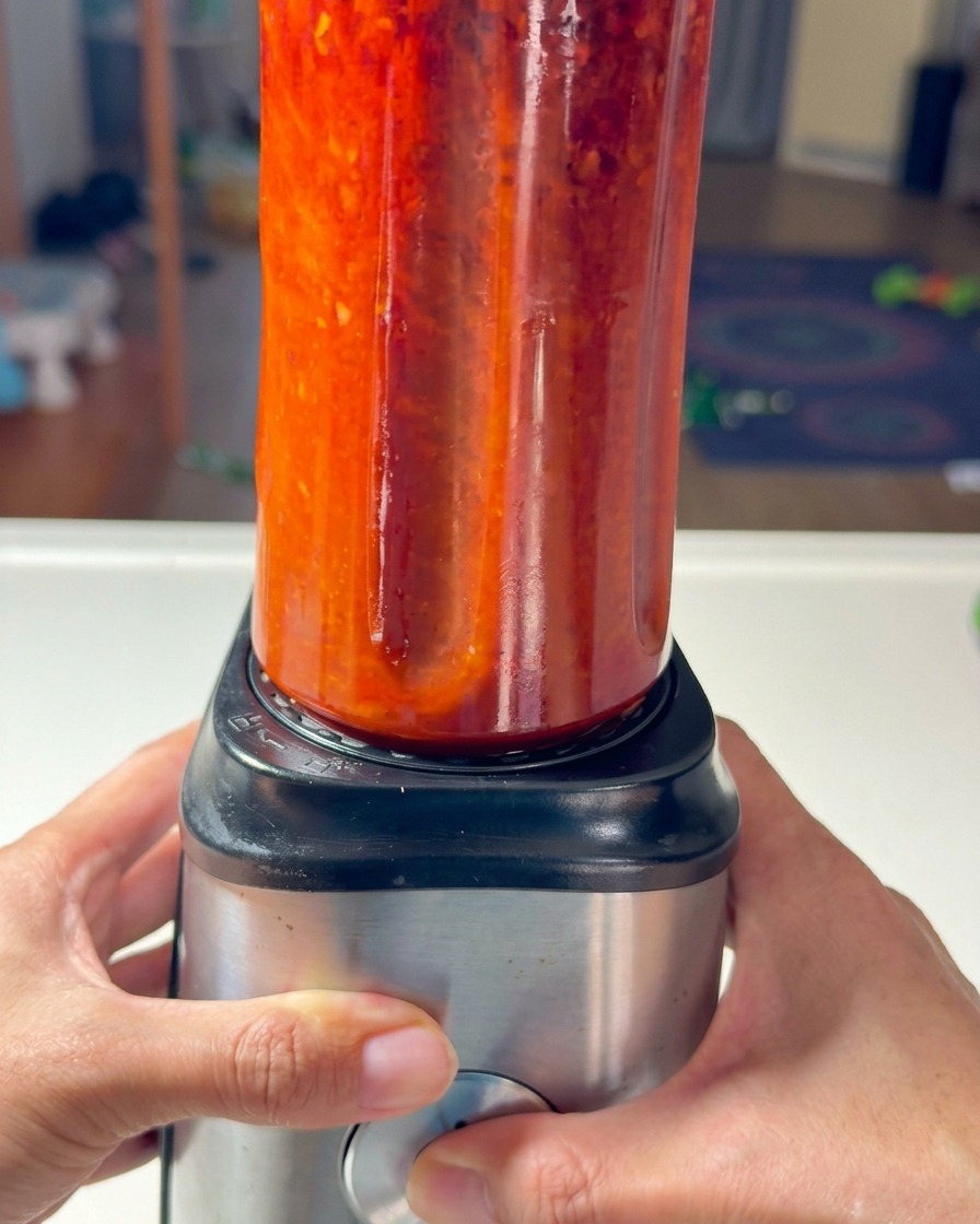Ein Mixbecher mit roter Chilipaste wird auf eine Basis gesetzt.