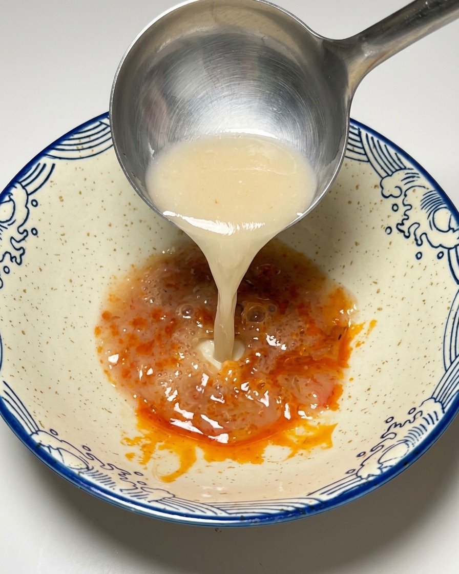 Cremige Tonkotsu-Brühe wird über die Chilipaste gegossen.