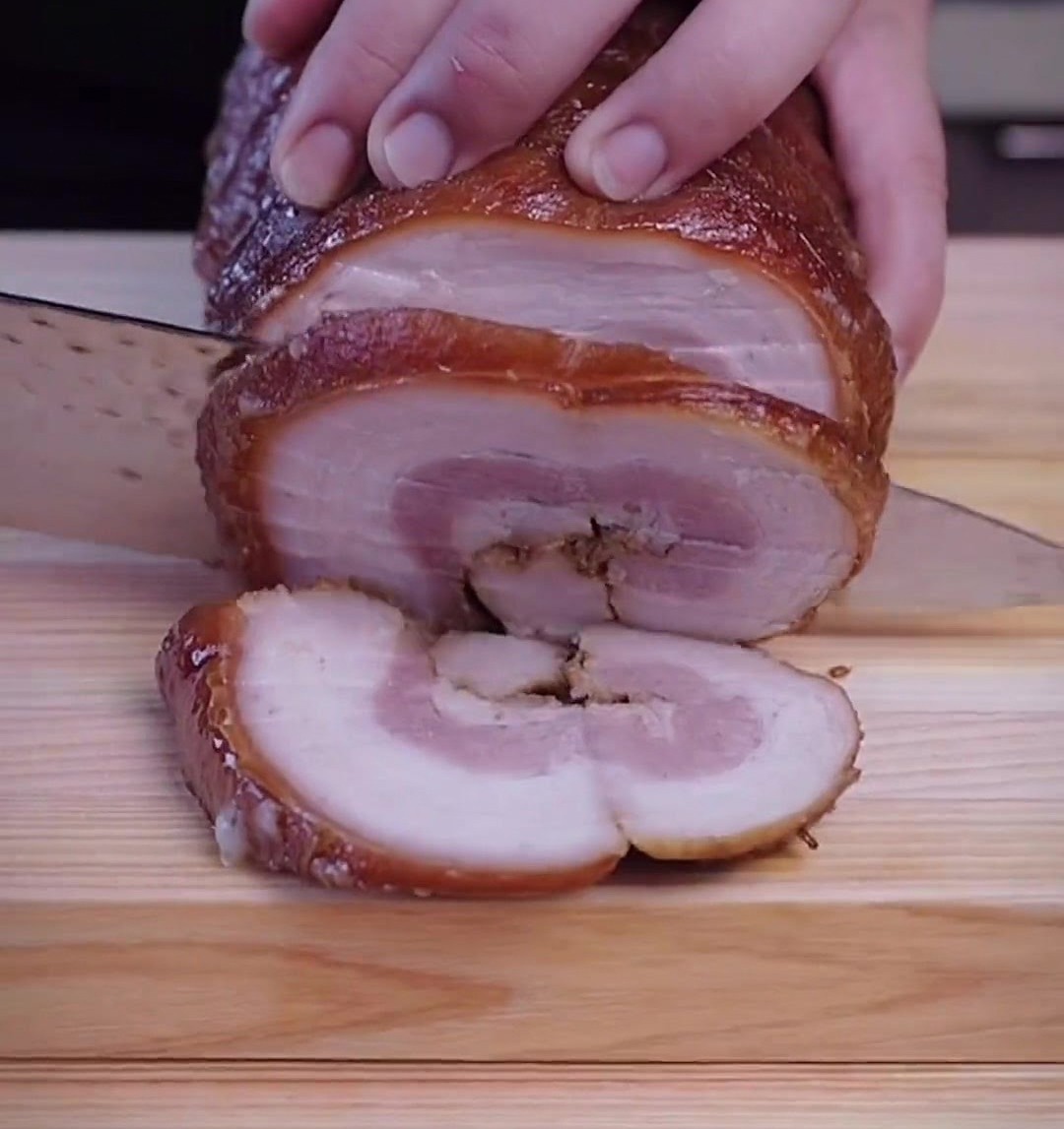 Hände schneiden die kalte Chashu-Rolle auf einem Holzbrett vorsichtig in dicke Scheiben.
