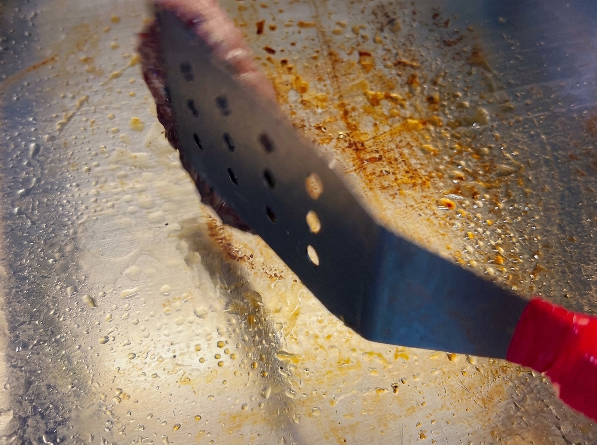 Ein Pfannenwender hebt ein Patty an, das auf der Unterseite eine dunkelbraune Kruste zeigt.