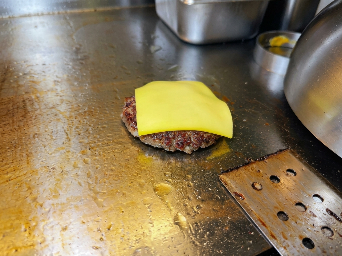 Eine Scheibe gelber Käse schmilzt auf dem heißen Fleisch-Patty.