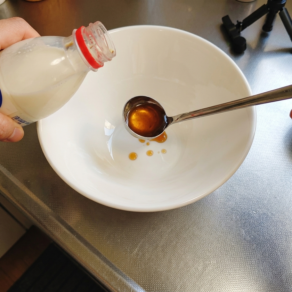Bernsteinfarbene flüssige Tare-Würzung wird aus einer Flasche in eine Metallkelle gegossen, die über eine weiße Servierschüssel gehalten wird.