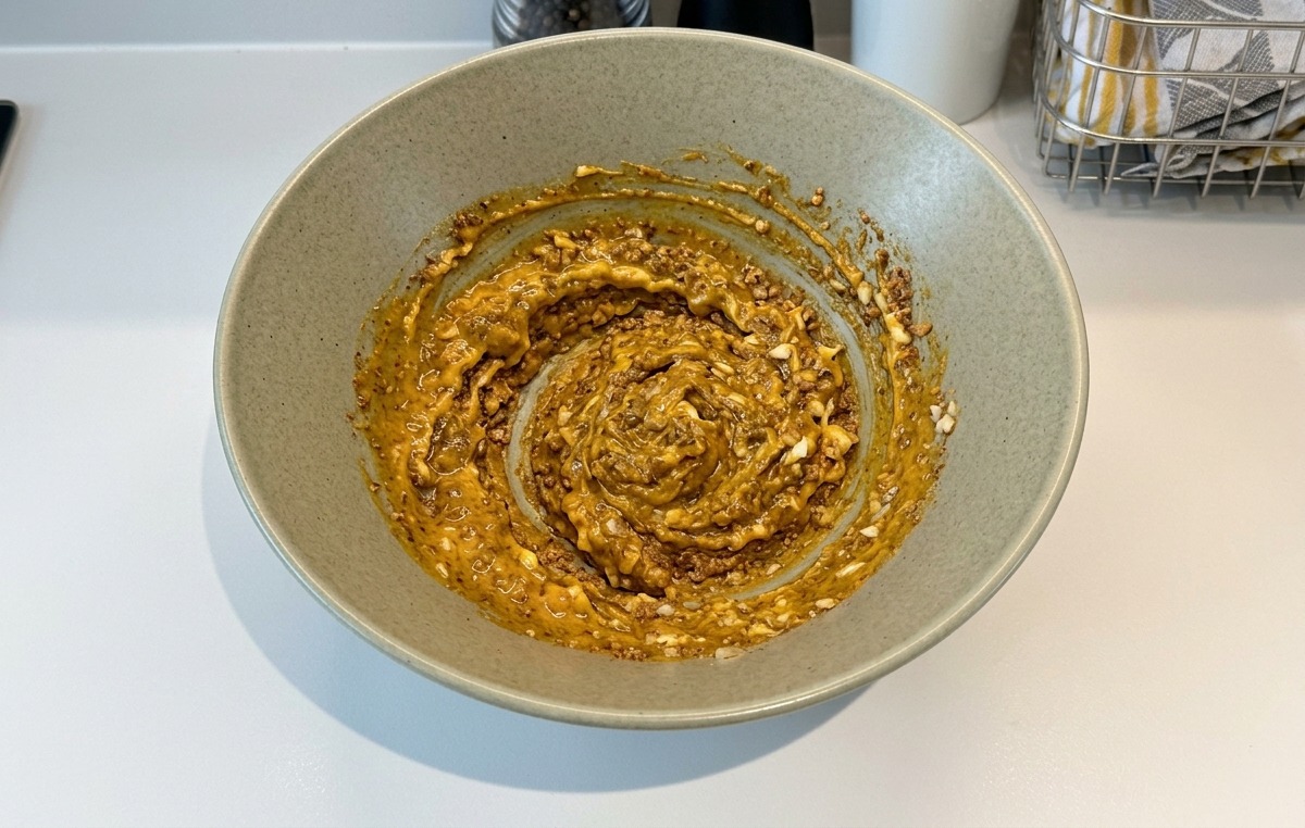 Eine dicke, braune, gut durchmischte Paste aus Gewürzen, Mayonnaise und Knoblauch wird in einer Keramikschüssel verrührt.