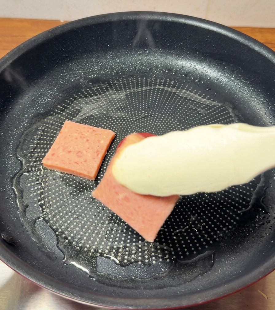 Rosa Frühstücksfleisch-Scheiben brutzeln in einer Pfanne, eine Seite ist bereits goldbraun gebraten.