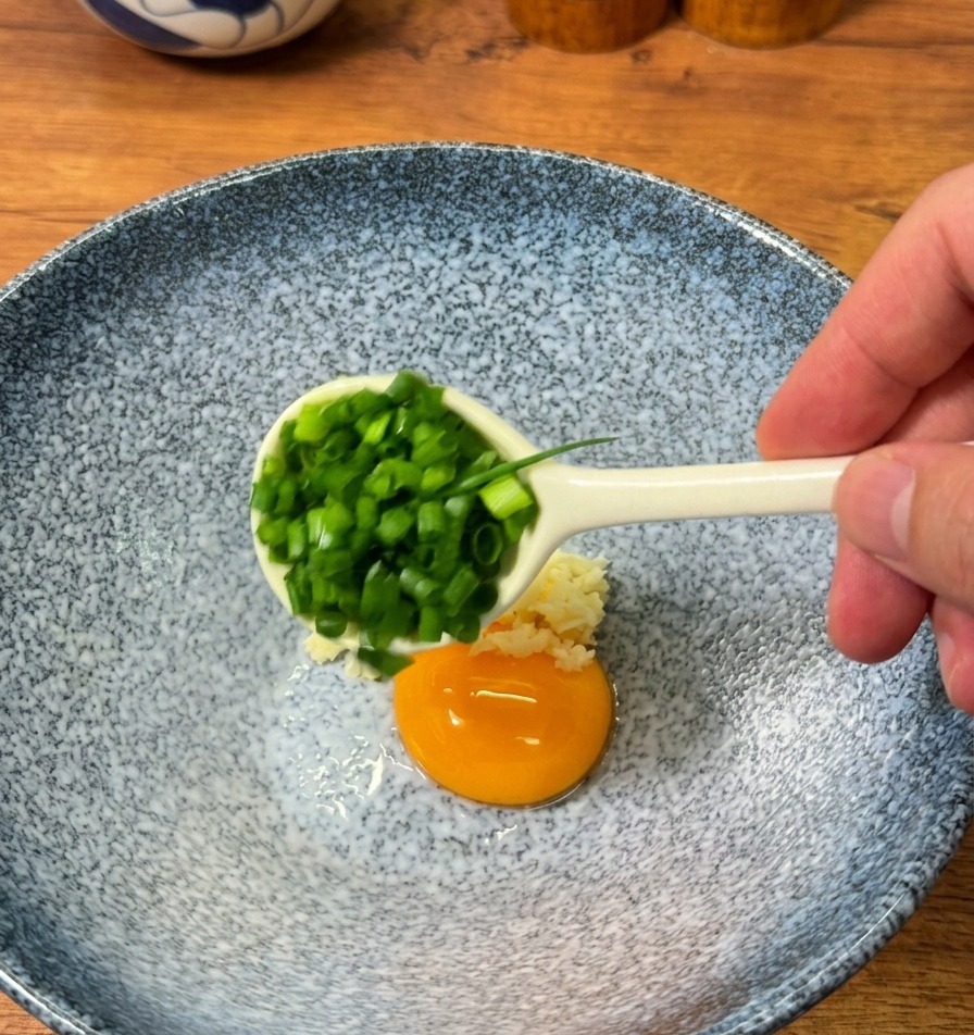Frühlingszwiebeln werden zu Knoblauch, Würzpulver und einem rohen Eigelb in eine Schüssel gegeben.