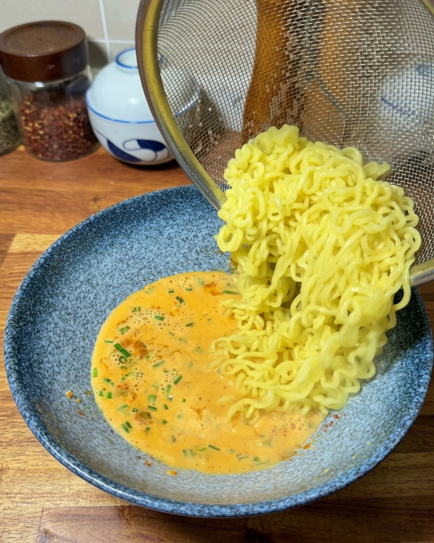 Gegarte Ramen-Nudeln gleiten aus einem Sieb direkt in die vorbereitete cremige Brühe.