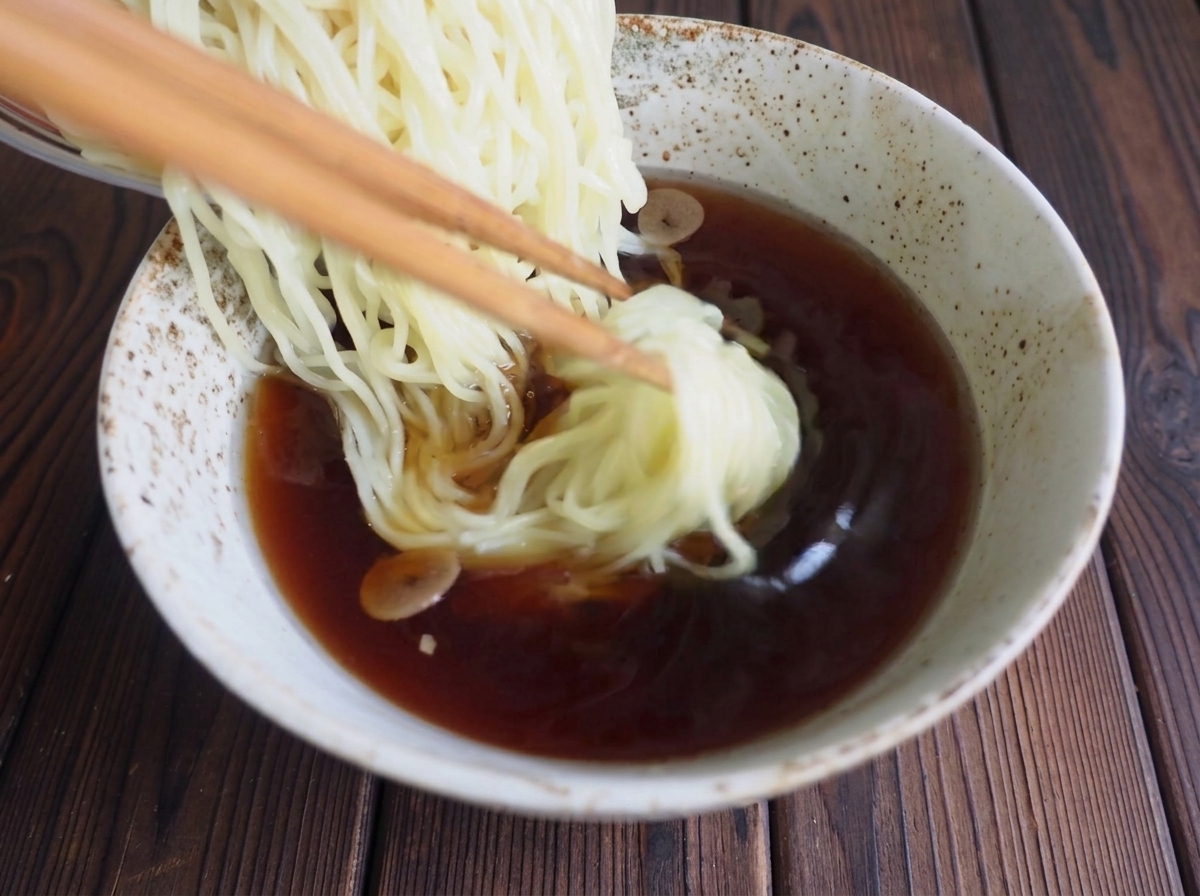 Nudeln werden vorsichtig in die Schale mit der dunklen Ramen-Suppe gelegt.