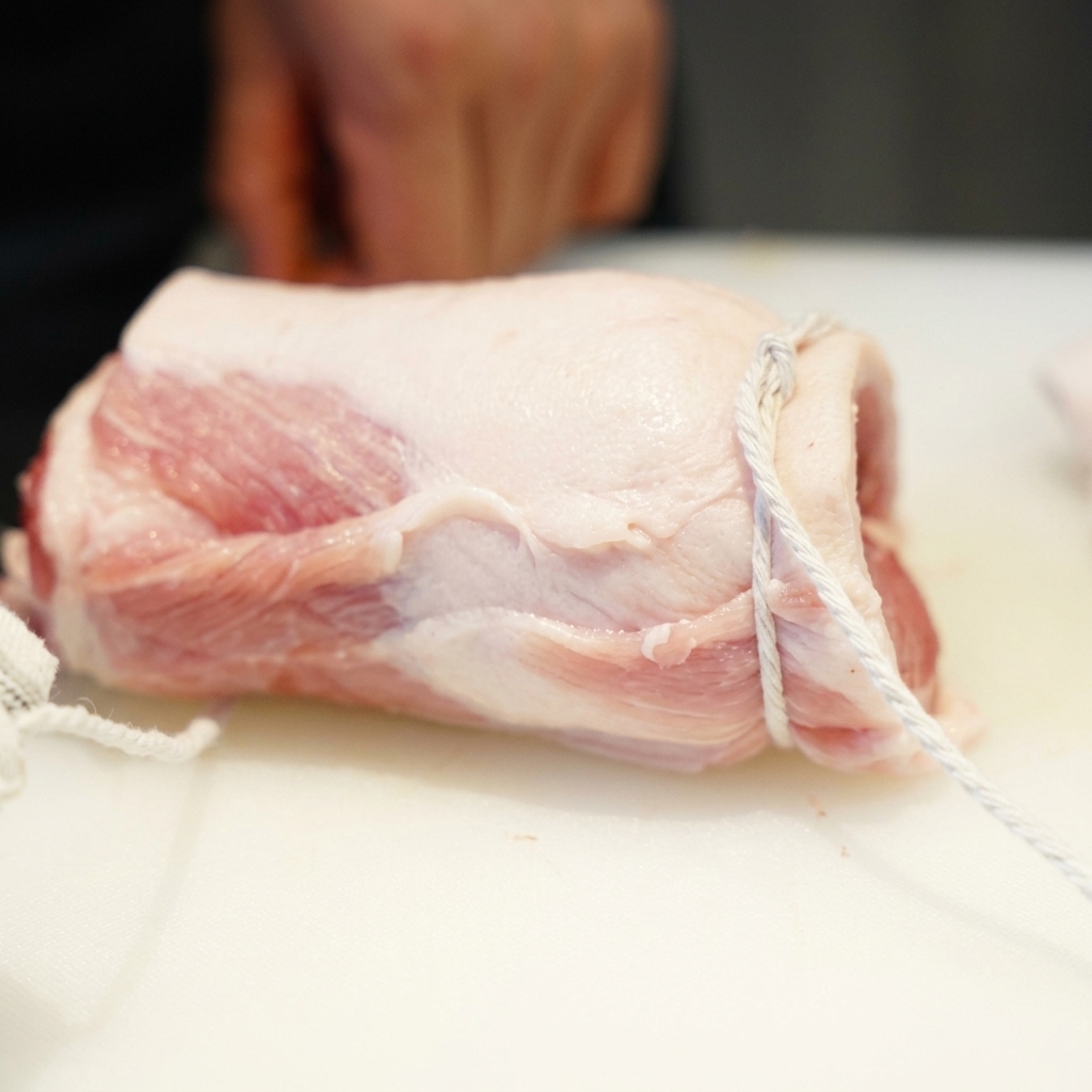 Ein fest zu einem Zylinder gerollter Schweinebauch, der mit weißem Küchengarn fixiert ist.