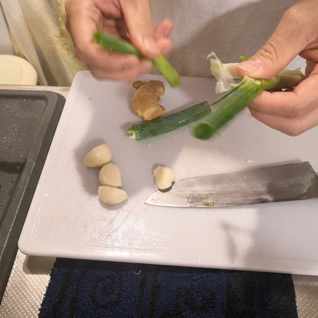 Hände bereiten das Grüne von Frühlingszwiebeln auf einem weißen Schneidebrett neben einem Küchenmesser vor.