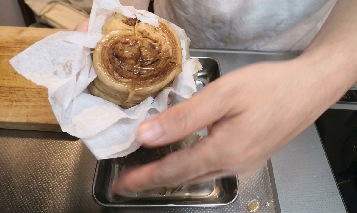 Hände tupfen den geschmorten Schweinebauch mit Küchenpapier auf einem Metallblech trocken.