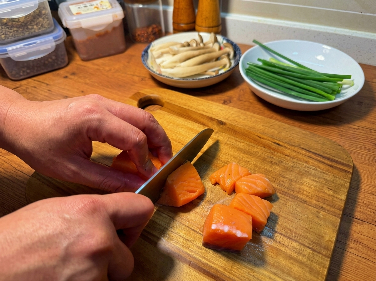 Hände schneiden ein frisches Lachsfilet auf einem Holzbrett in gleichmäßige Stücke.