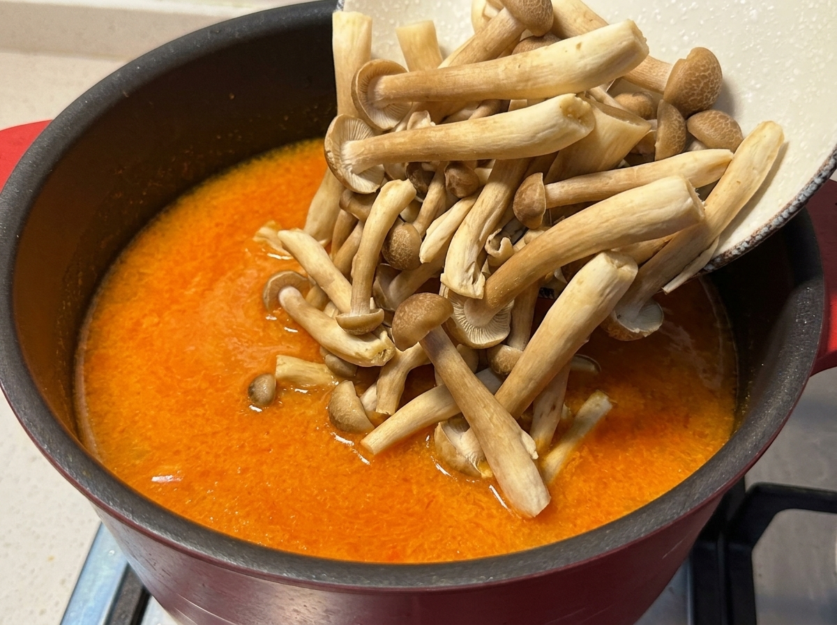 Braune Buchenpilze werden in die köchelnde orangefarbene Miso-Brühe gegeben.