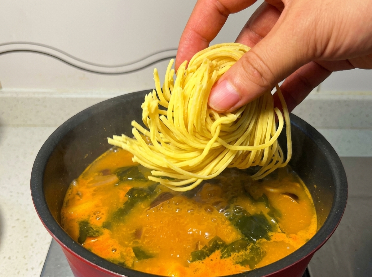 Ein Nest frischer gelber Ramen-Nudeln wird in die kochende Suppe gegeben.
