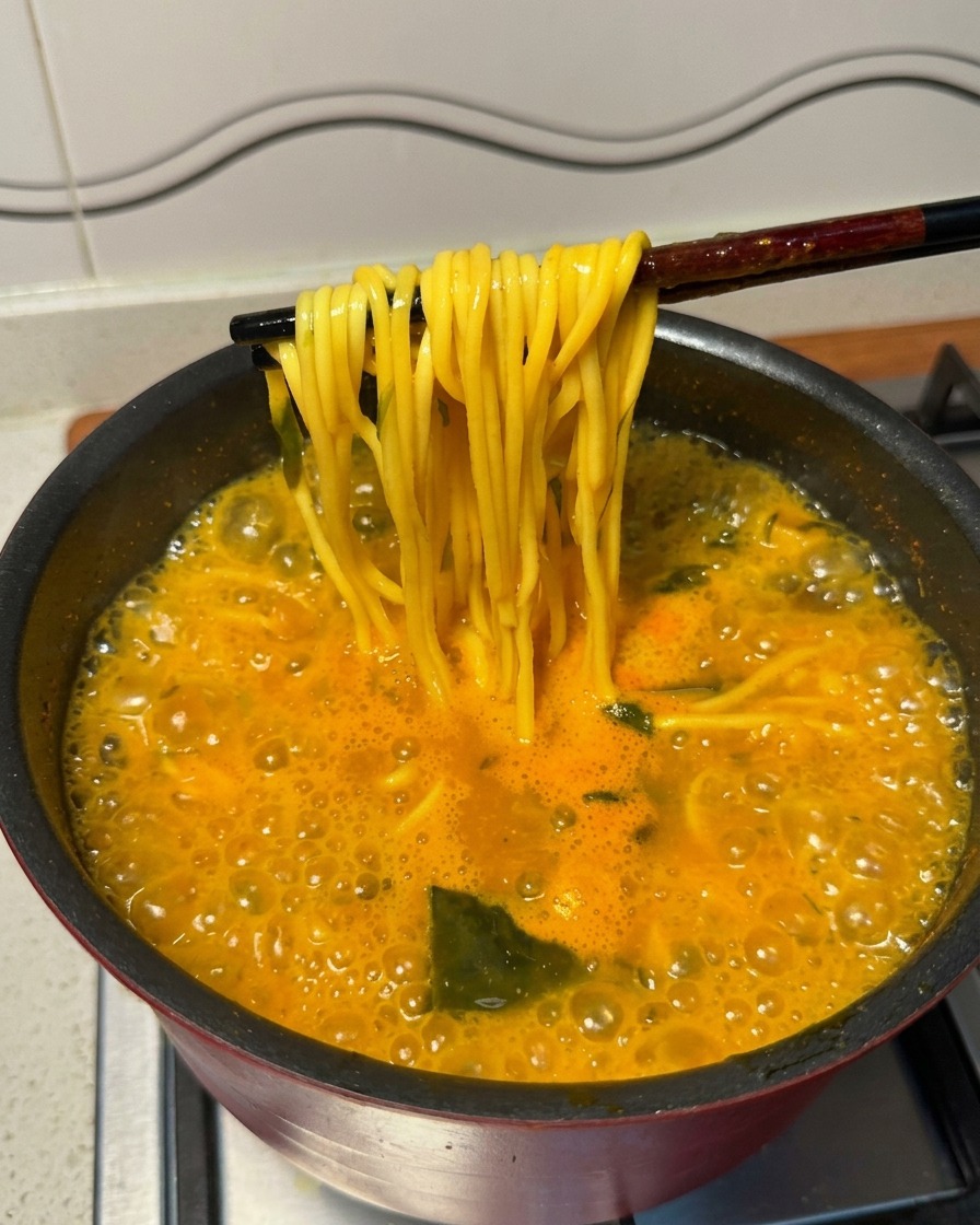 Stäbchen heben fertige Ramen-Nudeln aus dem sprudelnd kochenden Topf.