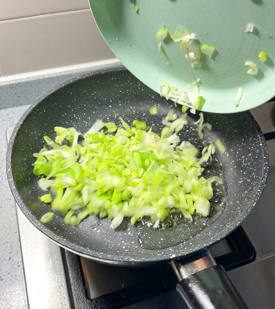 Gehackte Frühlingszwiebeln werden von einem hellgrünen Teller in eine heiße Pfanne gegeben.