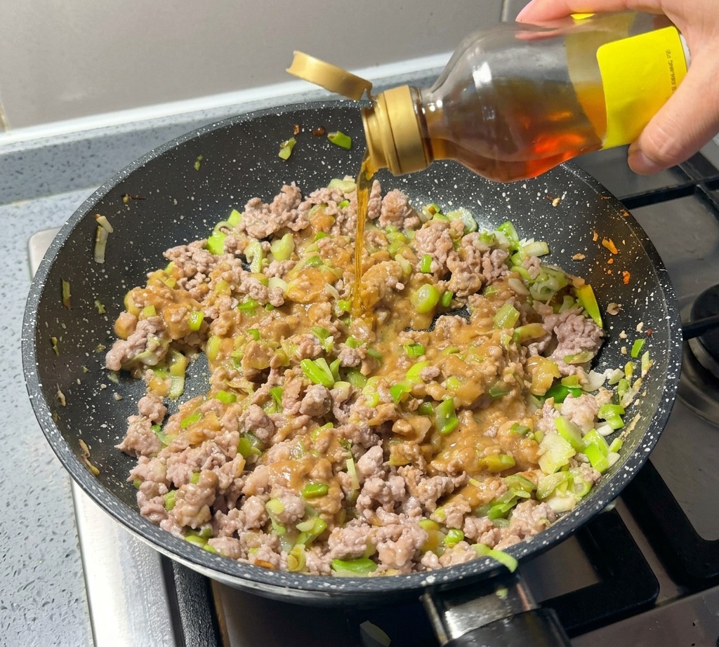 Sesamöl wird direkt aus der Flasche über die Fleischmischung in der Pfanne gegossen.