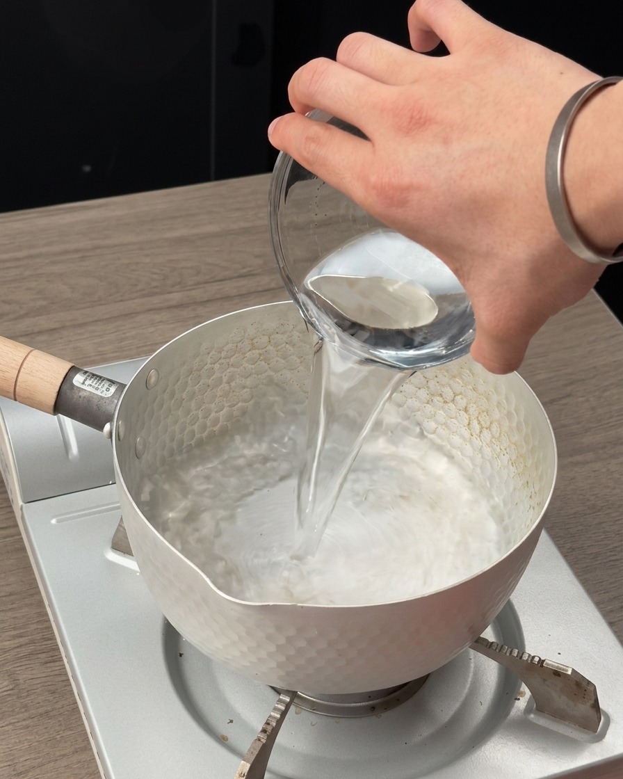 Wasser wird in einen kleinen Topf auf einem mobilen Kochfeld gegossen.
