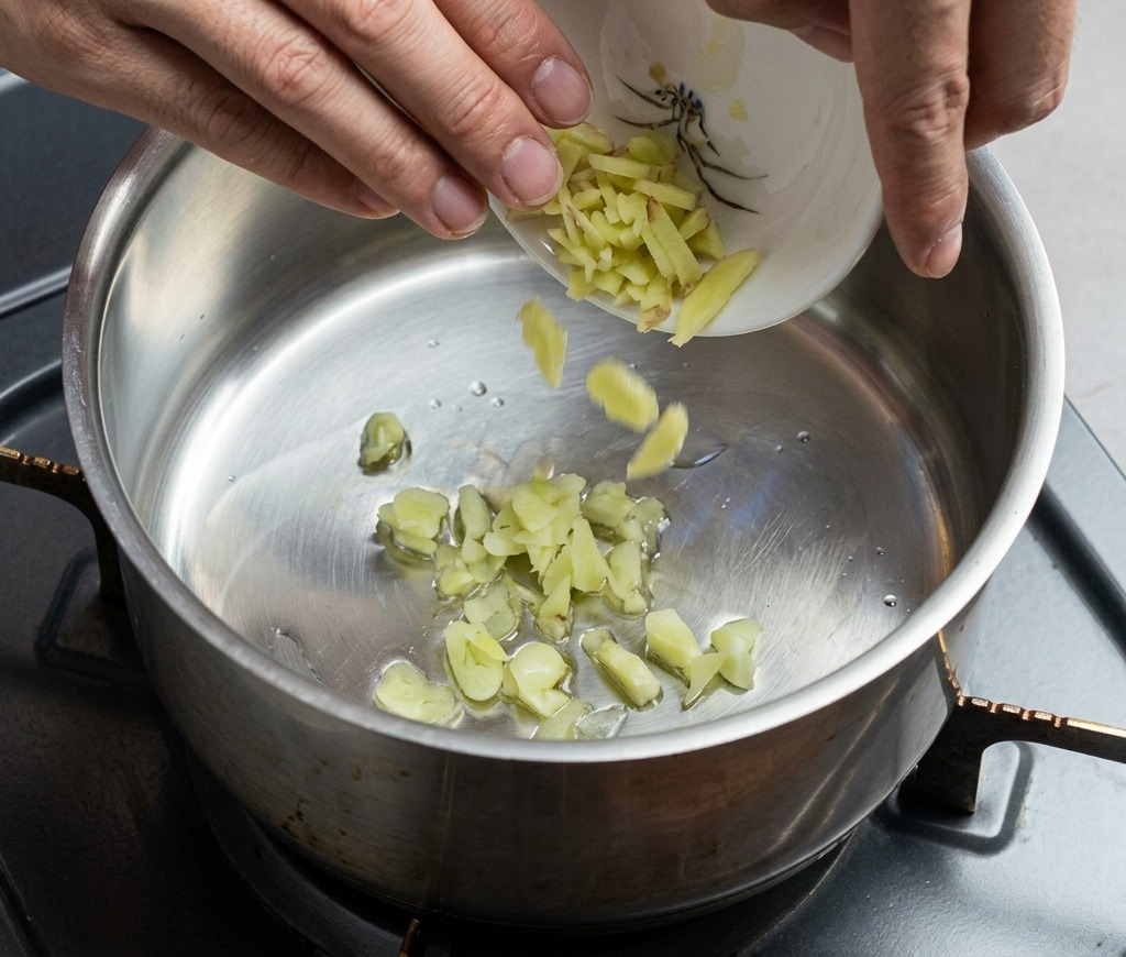 Gehackter Ingwer und Knoblauch werden aus einer kleinen Schale in einen heißen Edelstahltopf gegeben.
